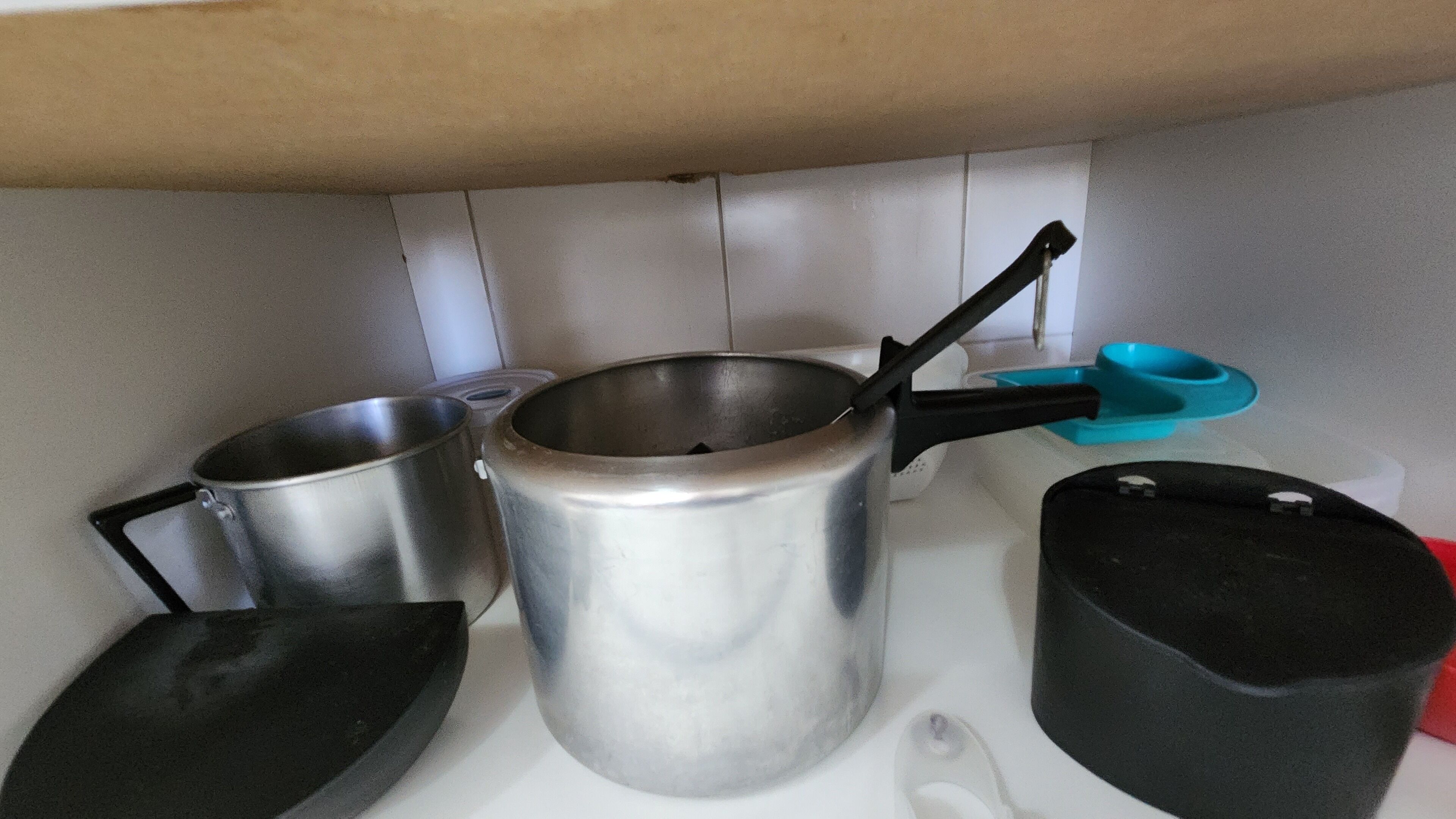 Ett kök med kastruller och stekpannor i rostfritt stål, en slev med blått handtag och en svart kastrull.