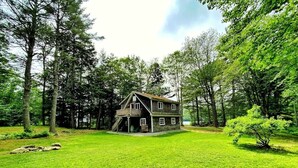 Une cabane en rondins à deux étages, dotée d’un balcon, entourée d’un paysage verdoyant et luxuriant et de grands arbres.