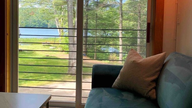 Une pièce dotée d’une porte-fenêtre coulissante donnant sur une terrasse, d’un canapé bleu avec un coussin et d’un luminaire suspendu.