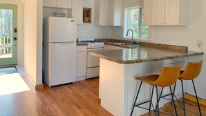 Une cuisine moderne avec des meubles blancs, un plan de travail en granit et deux tabourets de bar.