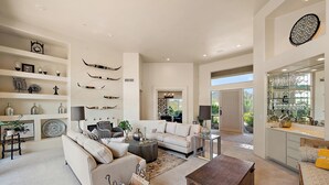 Un salon spacieux comprenant un canapé, une table basse et des objets de décoration. On y trouve également un coin repas avec un lustre, ainsi qu’une cuisine dotée d’une grande fenêtre.