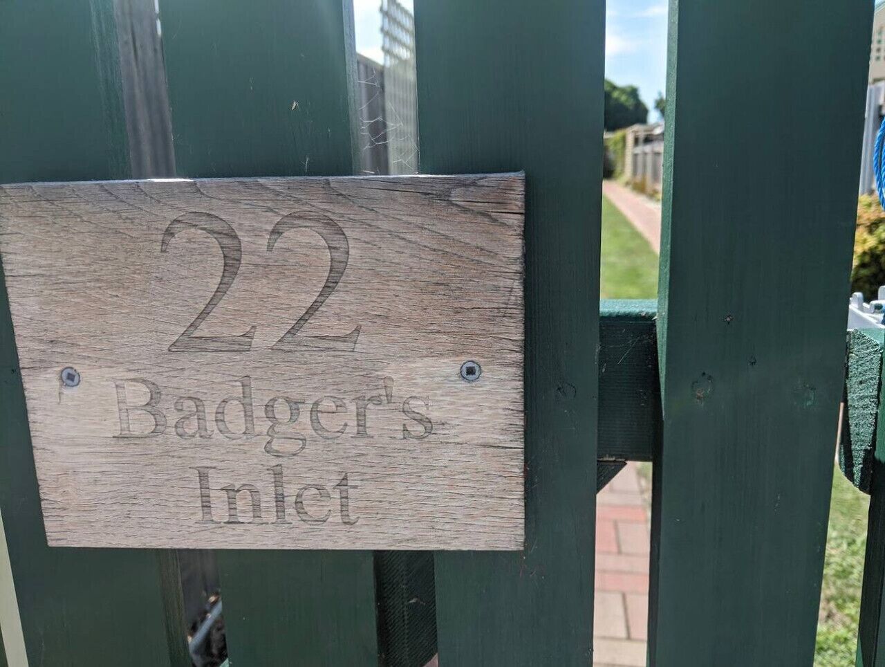 Une plaque en bois portant le numéro 22 et l’inscription « Badger’s Inlet », fixée sur un portail métallique vert.