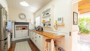 Une cuisine avec des meubles blancs, un plan de travail en bois, une cuisinière encastrée et une fenêtre donnant sur un jardin.