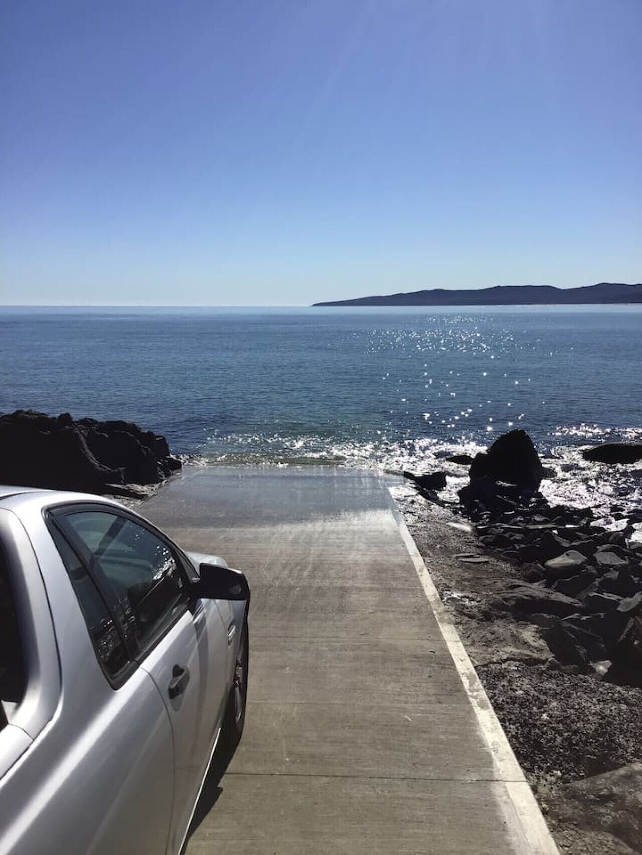 A coastal road with a car parked on the left, leading to a rocky shoreline.
