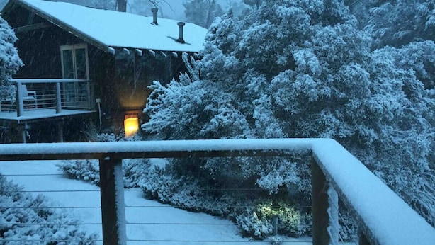 A wooden cabin with a snow-covered roof and a lit interior, surrounded by snow-laden trees. - Spacious Family Home in Devonport  (Devonport)