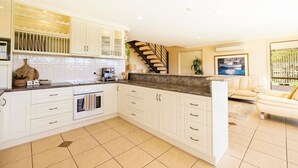 Une cuisine moderne avec des meubles blancs, un plan de travail foncé et un escalier menant à un espace de vie agrémenté d’un canapé blanc et d’un tableau.