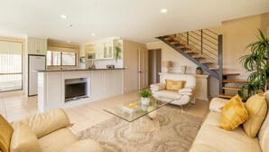 Un salon moderne avec une table basse en verre, des canapés de couleur beige et un escalier avec des marches en bois.