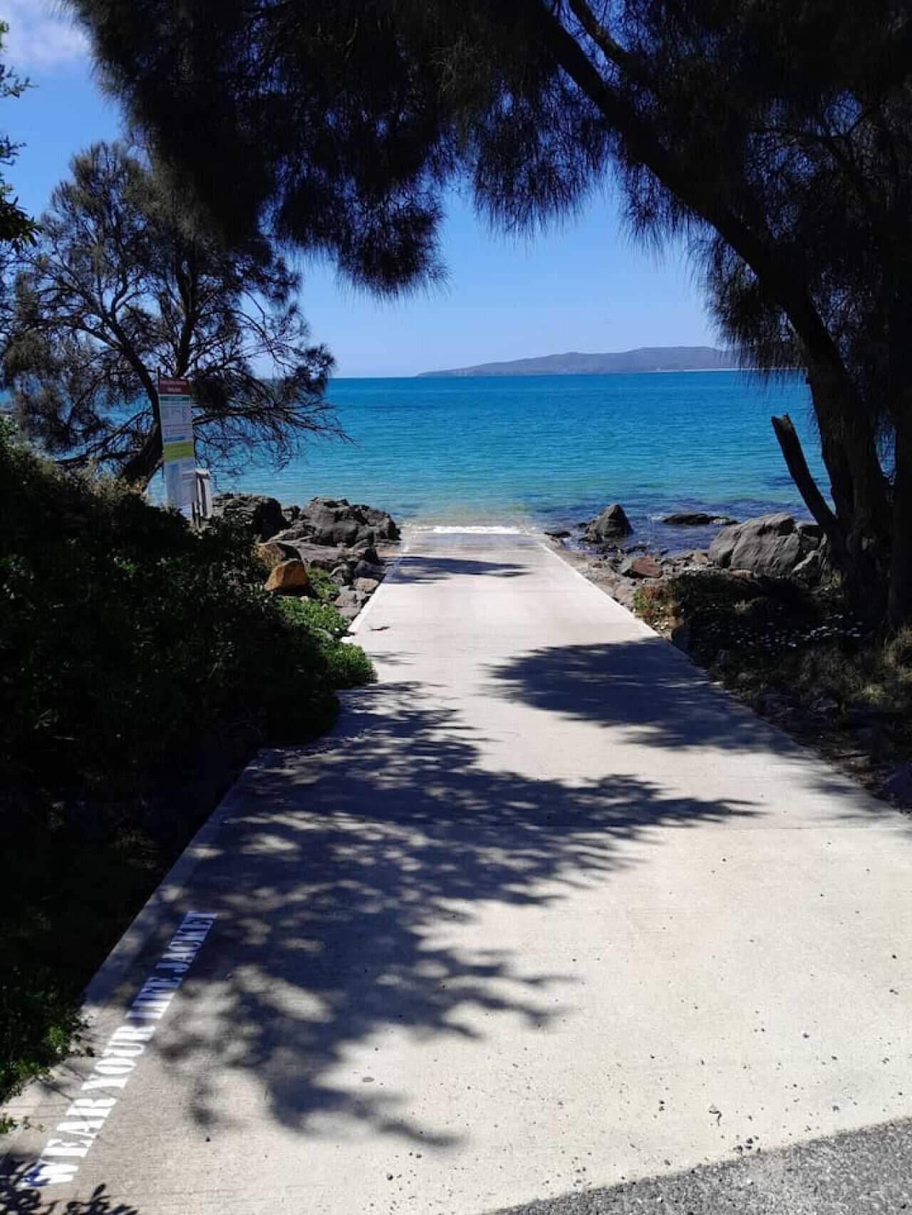 Un sendero pavimentado que conduce a una playa con aguas azules cristalinas y afloramientos rocosos.