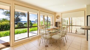 Un vaste espace dédié à la salle à manger, avec une table et des chaises en verre, de grandes fenêtres offrant une vue sur la verdure et un paysage lointain.