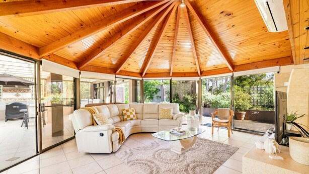 Un salon moderne avec un plafond en bois, un canapé blanc, une table basse en verre et une vue sur l’extérieur.
