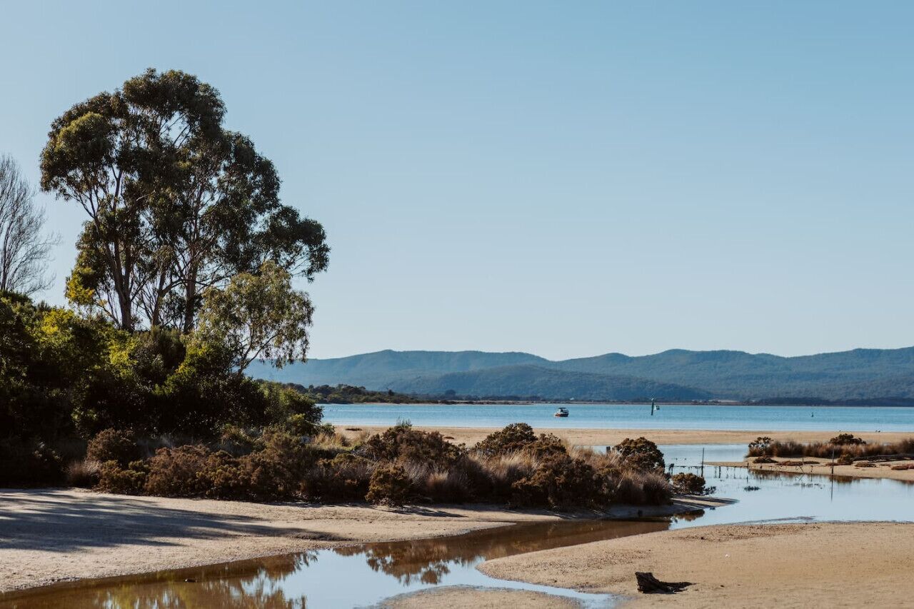 Ein Strand mit klarem Wasser, einem Boot und fernen Bergen.