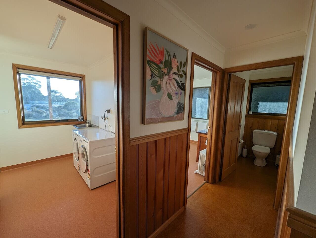 A laundry room with a washing machine, a sink, and a wooden wall with a framed painting.