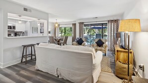 A modern living room with a sofa, dining area, and kitchen. - 266 Turnberry Village @ Palmetto Dunes | Golf View | Walk to Beach | Pool Access (Hilton Head Island)