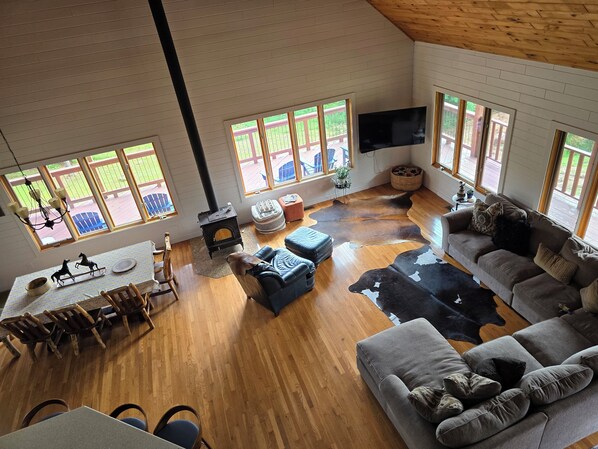 A spacious living room with a large black wood-burning stove, a gray sofa, a leather chair, and a dining area with wooden chairs and a table. - Wisconsin Dells Gathering for 15 Guests/7.5 Acres/5 mins from Downtown Dells (Wisconsin Dells)