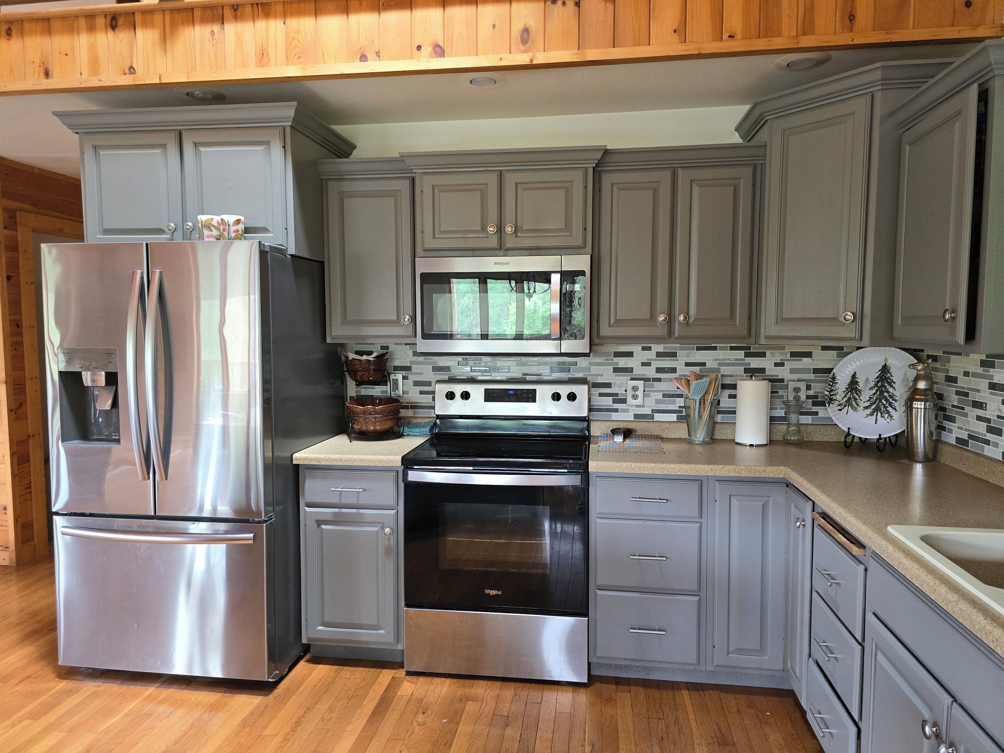 A modern kitchen with grey cabinets, stainless steel appliances, and a wooden floor.