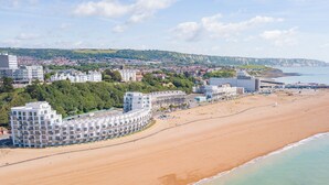 A coastal hotel with a curved building, beachfront location, and a view of the sea and distant hills.