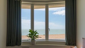 A room with a bay window overlooking a beach.