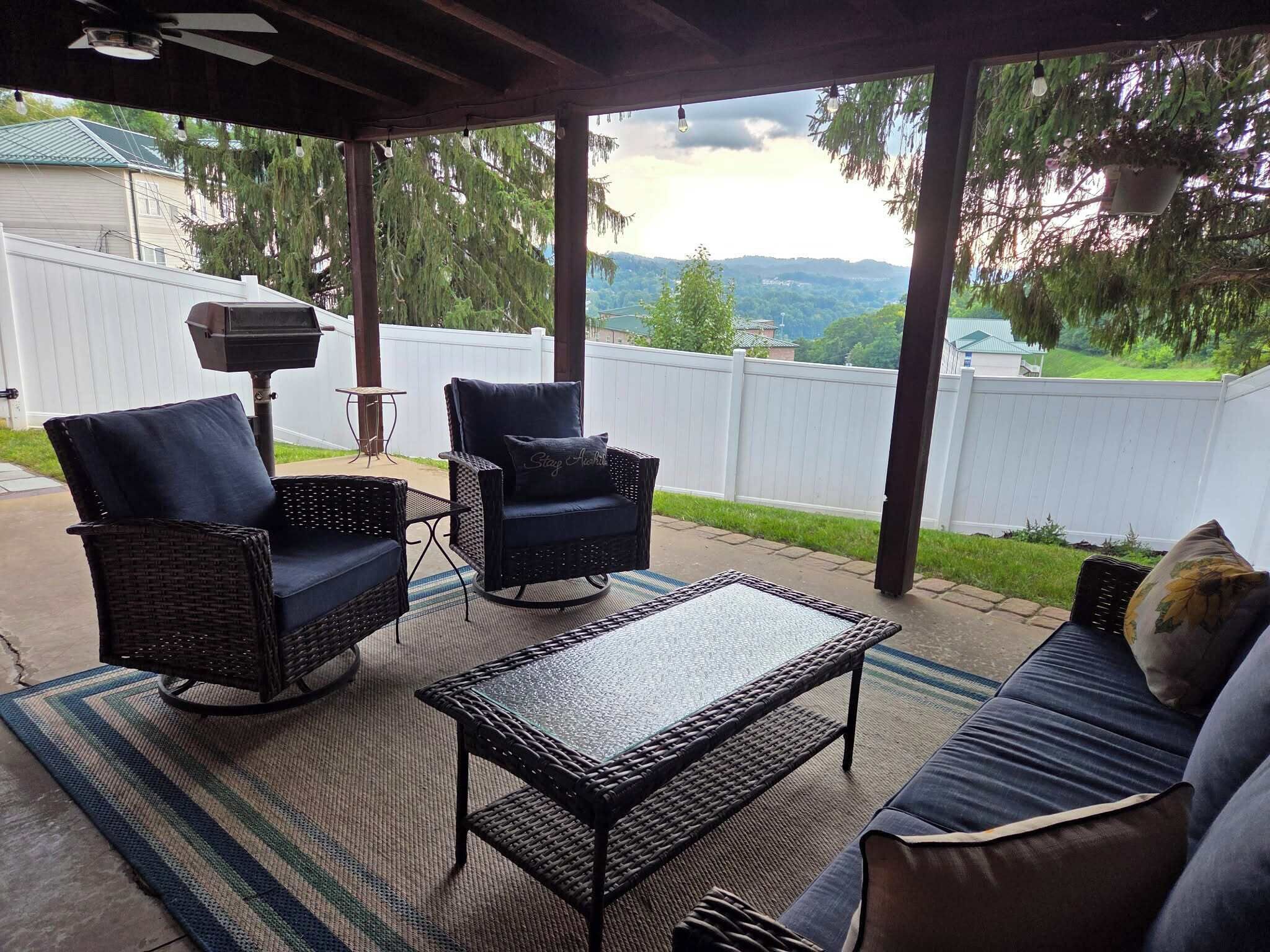 An outdoor patio with wicker furniture, a grill, and a view of a green landscape.