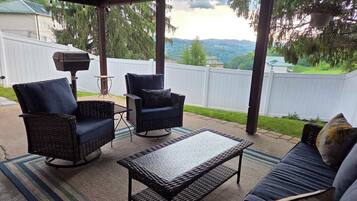 An outdoor patio with wicker furniture, a grill, and a view of a green landscape.