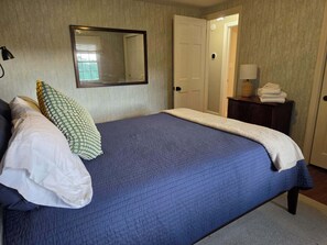 A bedroom with a bed, pillows, a mirror, a dresser, and a door. - Charming retro house on University Ave, walking distance from WVU Stadium. (Morgantown)