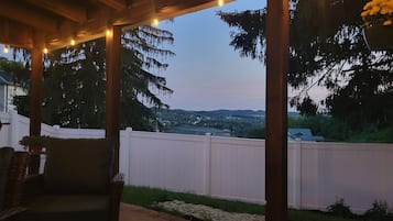 An outdoor patio with string lights, a white fence, and a view of a hilly landscape.