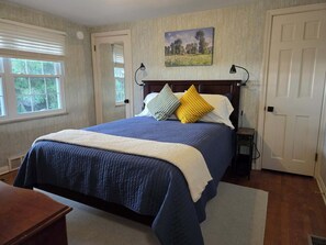 A bedroom with a bed, a painting on the wall, and a door.