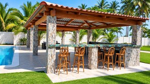 Un bar junto a la piscina con pilares de piedra, techo de azulejos y sillas de mimbre.