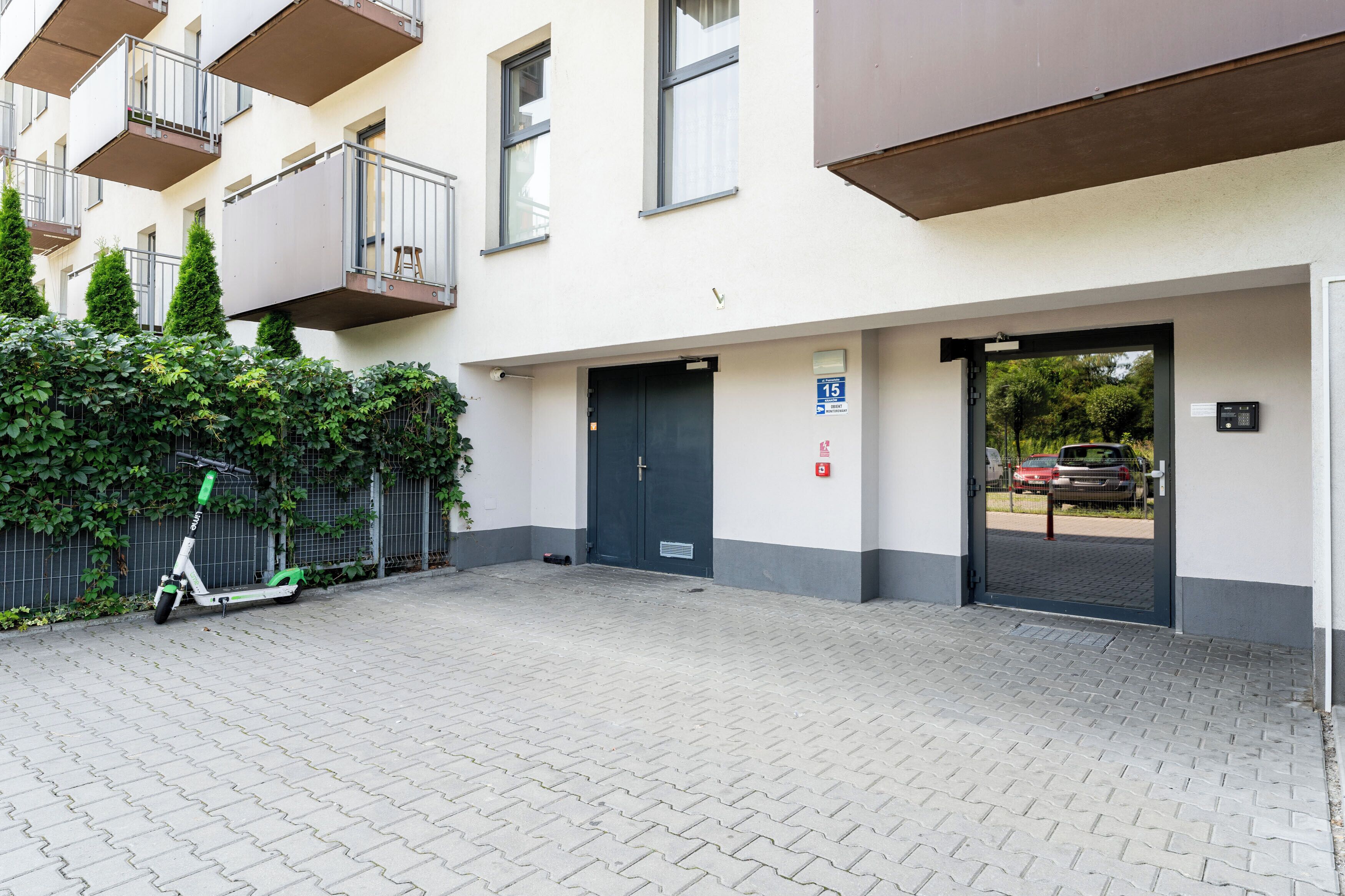 Une entrée d’immeuble avec une allée pavée, un scooter et une voiture garés à l’extérieur.