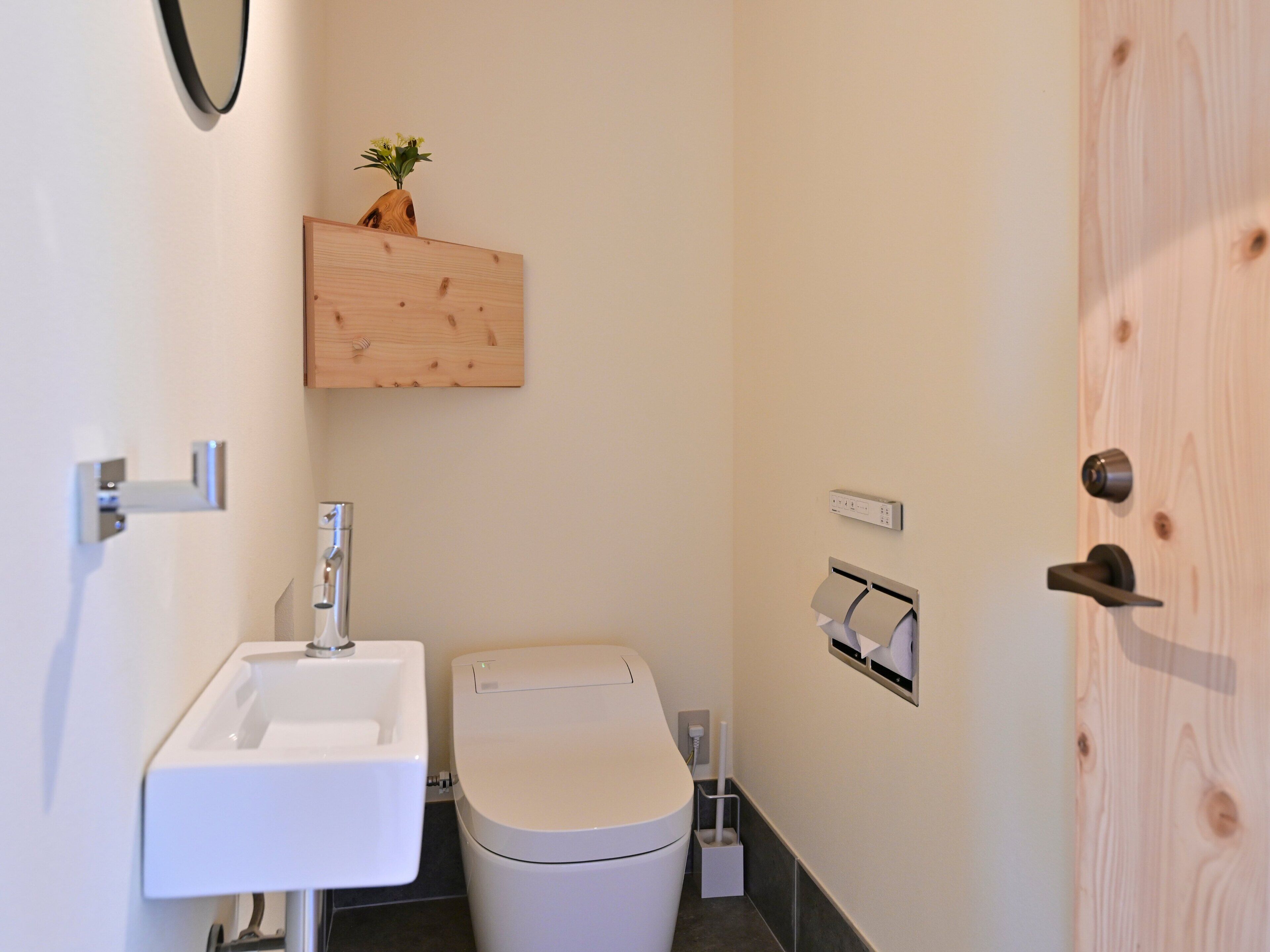 A small bathroom with a white sink, toilet, and a wooden shelf above the toilet.