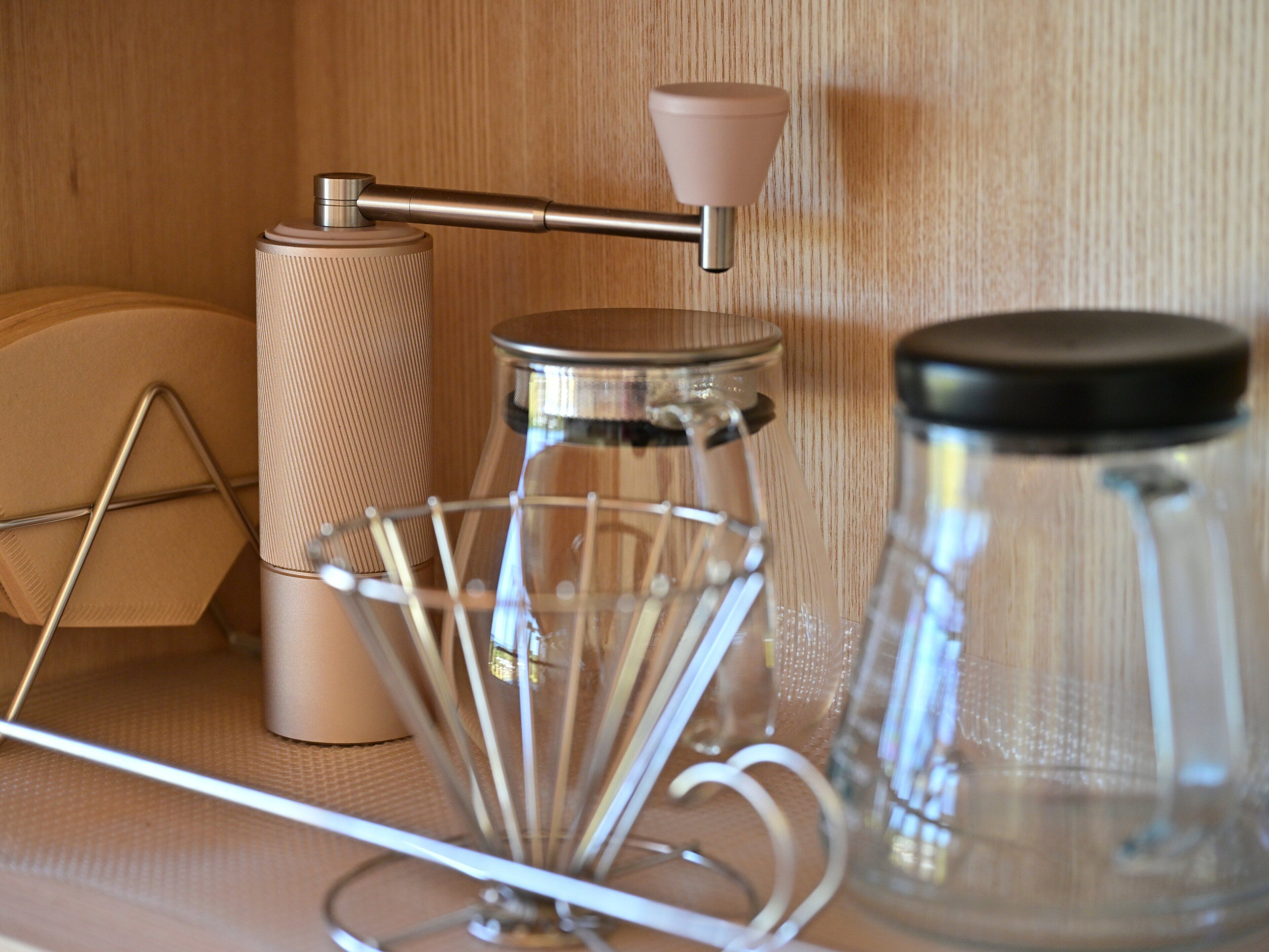 A kitchen area with a coffee maker, a glass jar, and a metal container on a wooden shelf.