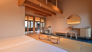 A bedroom with a large bed, a wooden ceiling, a small table with a bench, a mirror, and a view of the outdoors. - Ishigaki hills (Ishigaki)