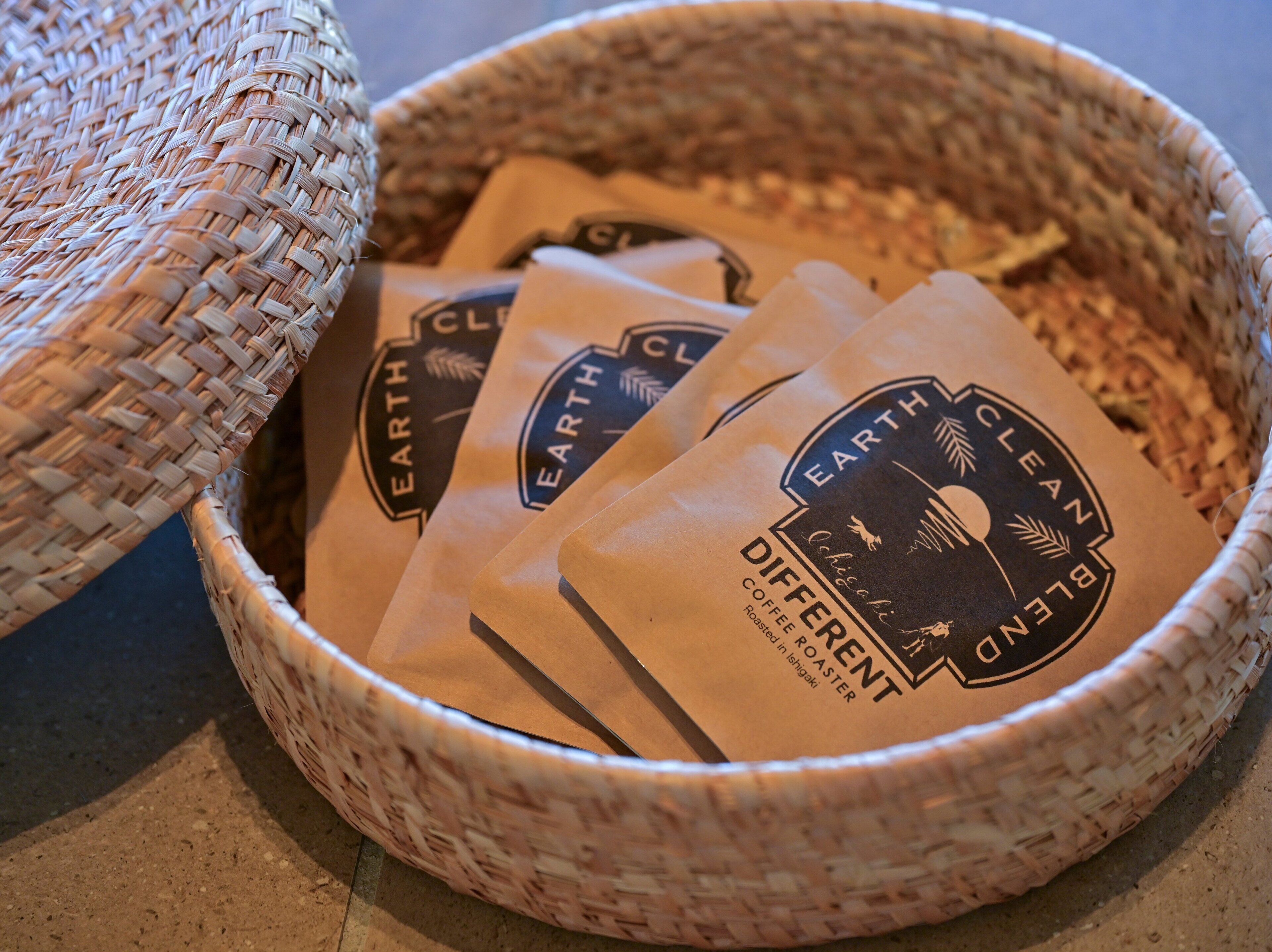 Una cesta tejida llena de bolsas de café con la etiqueta 'Earth Clean Planet'.