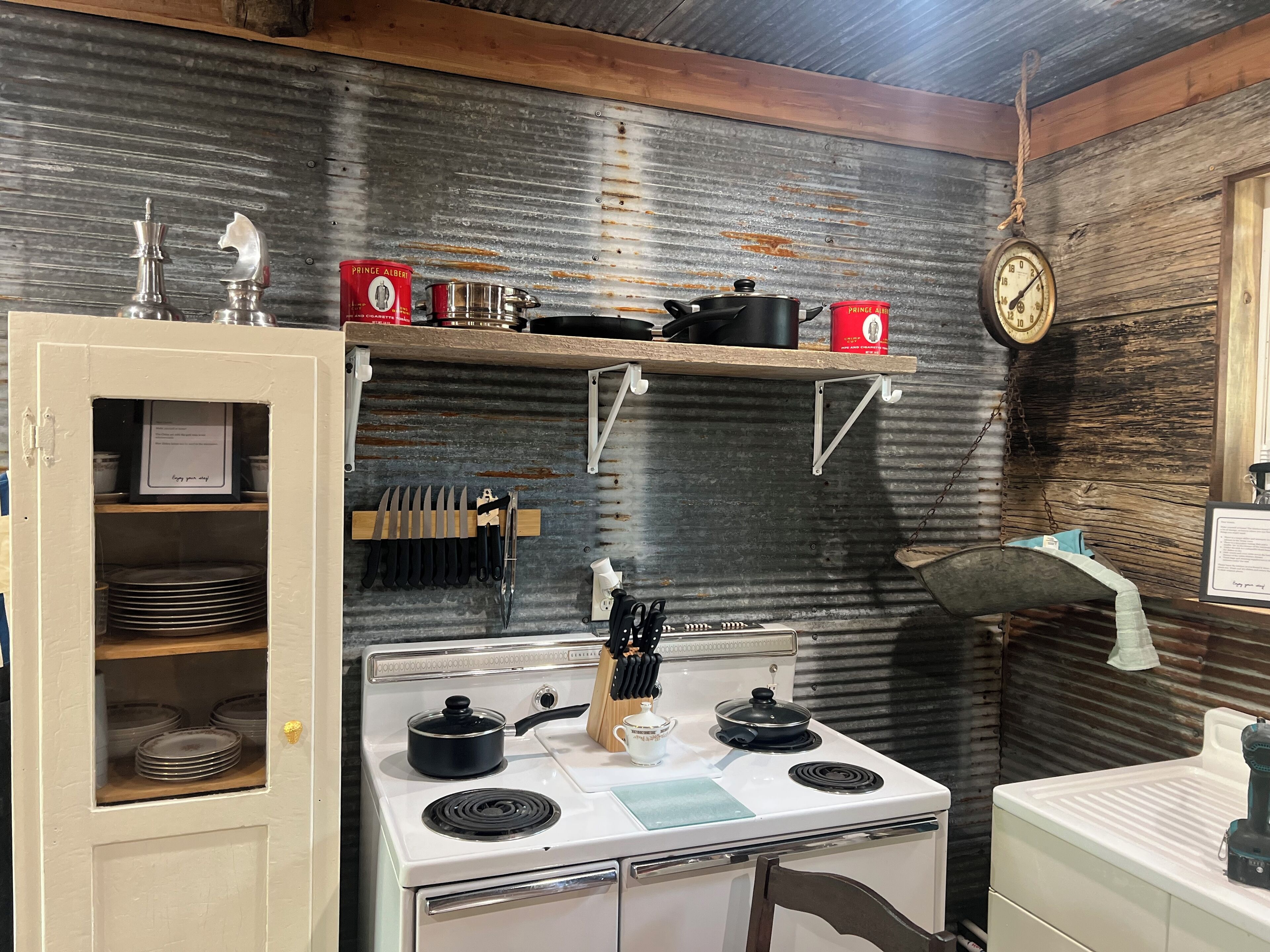 A kitchen with a stove, pots, a clock, and a shelf with items.