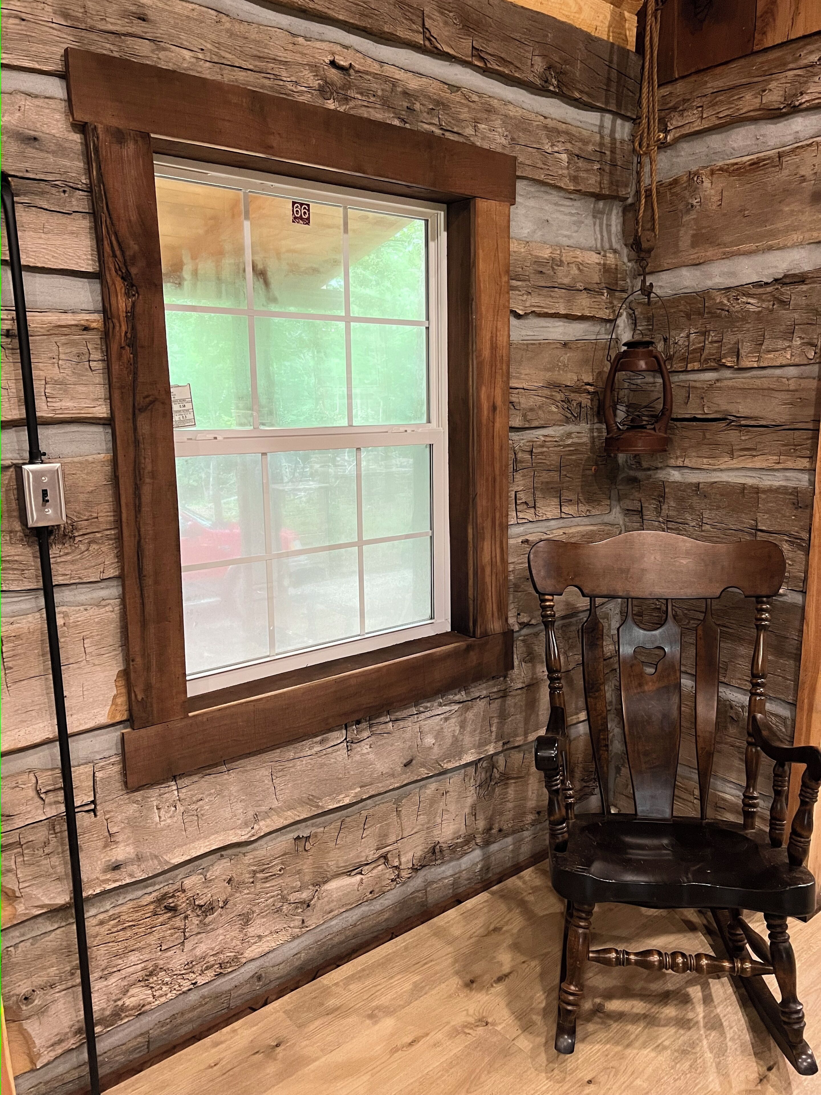 Interno di una baita rustica con un'ampia finestra, una sedia di legno e una lanterna.