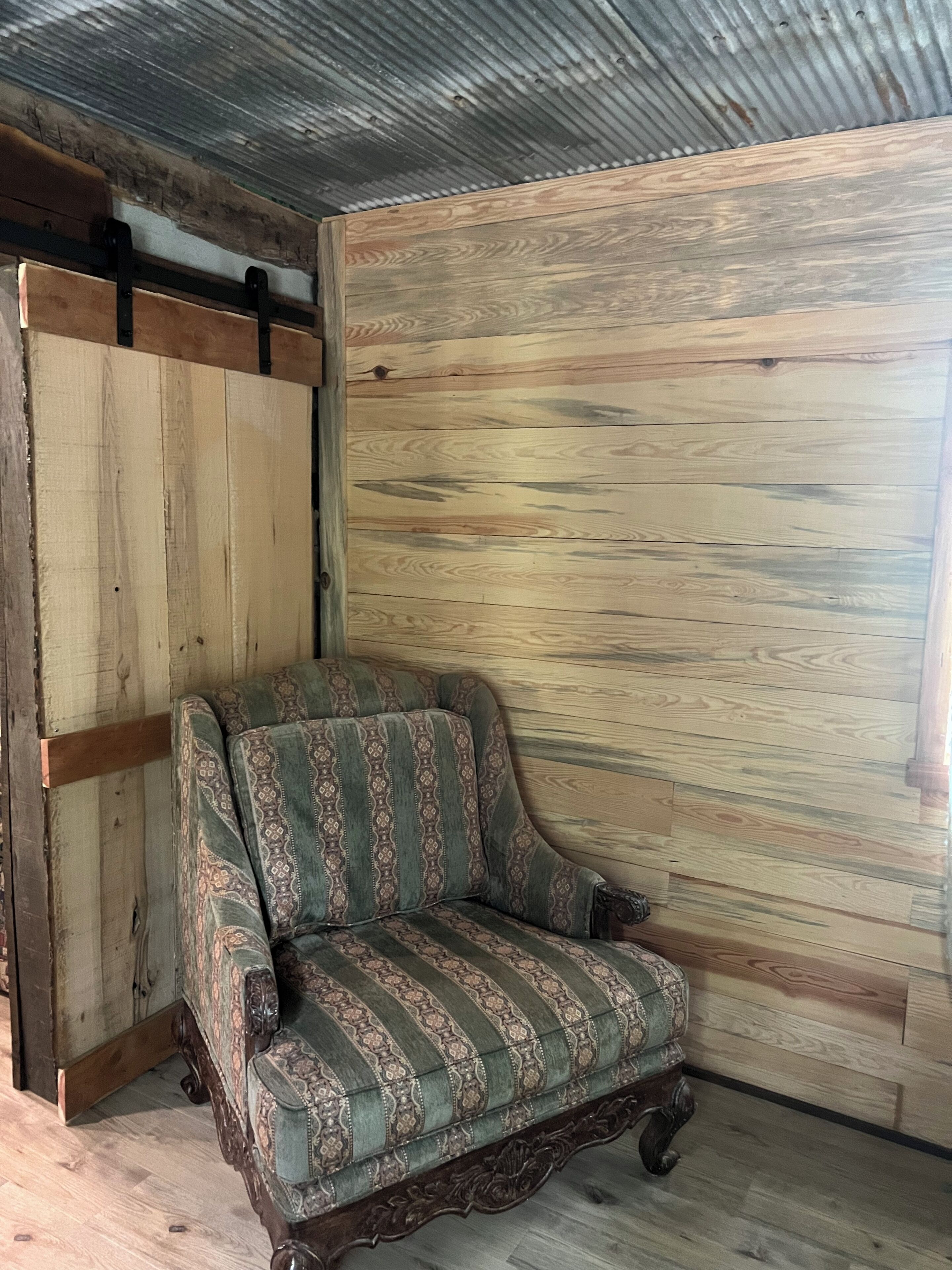 A vintage armchair with patterned upholstery against a wooden wall in a room with a corrugated metal ceiling.
