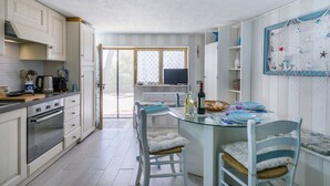 Une cuisine compacte dotée d’un îlot central, d’un coin repas avec des chaises et d’une grande fenêtre qui laisse entrer la lumière naturelle.
