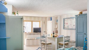 Une petite pièce comprenant un lit, un bureau et une chaise. Il y a une télévision sur le bureau, ainsi qu’une fenêtre avec des rideaux.