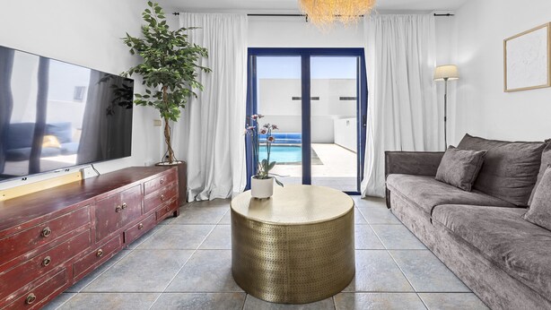 Ein modernes Wohnzimmer mit einem Flachbildfernseher, einem runden Couchtisch, einer Couch und einem großen Fenster mit Blick auf einen Pool.