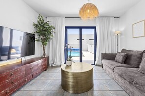 A modern living room with a flat-screen TV, a round coffee table, a sofa, and a large window with a view of a pool. - Villa Cartali Playa Blanca (Playa Blanca)