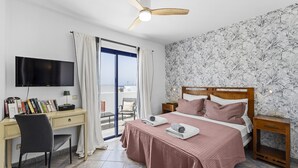 Ein Schlafzimmer mit Bett, Schreibtisch, Stuhl, Fernseher und Deckenventilator.