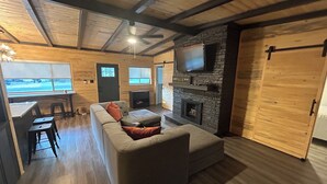 A cozy living room with a sofa, a fireplace, a TV mounted on a stone wall, and a wooden ceiling. - Gibson Getaway- Relax and Unwind (Wagoner)