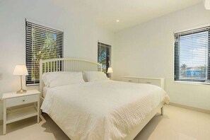 Ein Schlafzimmer mit einem großen Bett, zwei Nachttischen und Fenstern mit Jalousien.