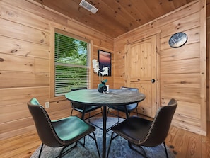 Un intérieur en bois avec une table ronde, quatre chaises, une horloge et une fenêtre avec des stores.