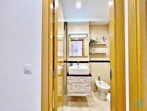 Et moderne badeværelse med en trædør, en hvid vask, en bidet og et spejl over vasken.