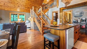 A spacious living area with a wooden ceiling, a staircase, and a kitchen area with a coffee bar.