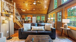 A spacious living area with a leather sofa, wooden ceiling, and large windows offering a view of the outdoors.