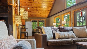 A cozy living room with a leather couch, wooden ceiling, and large windows.