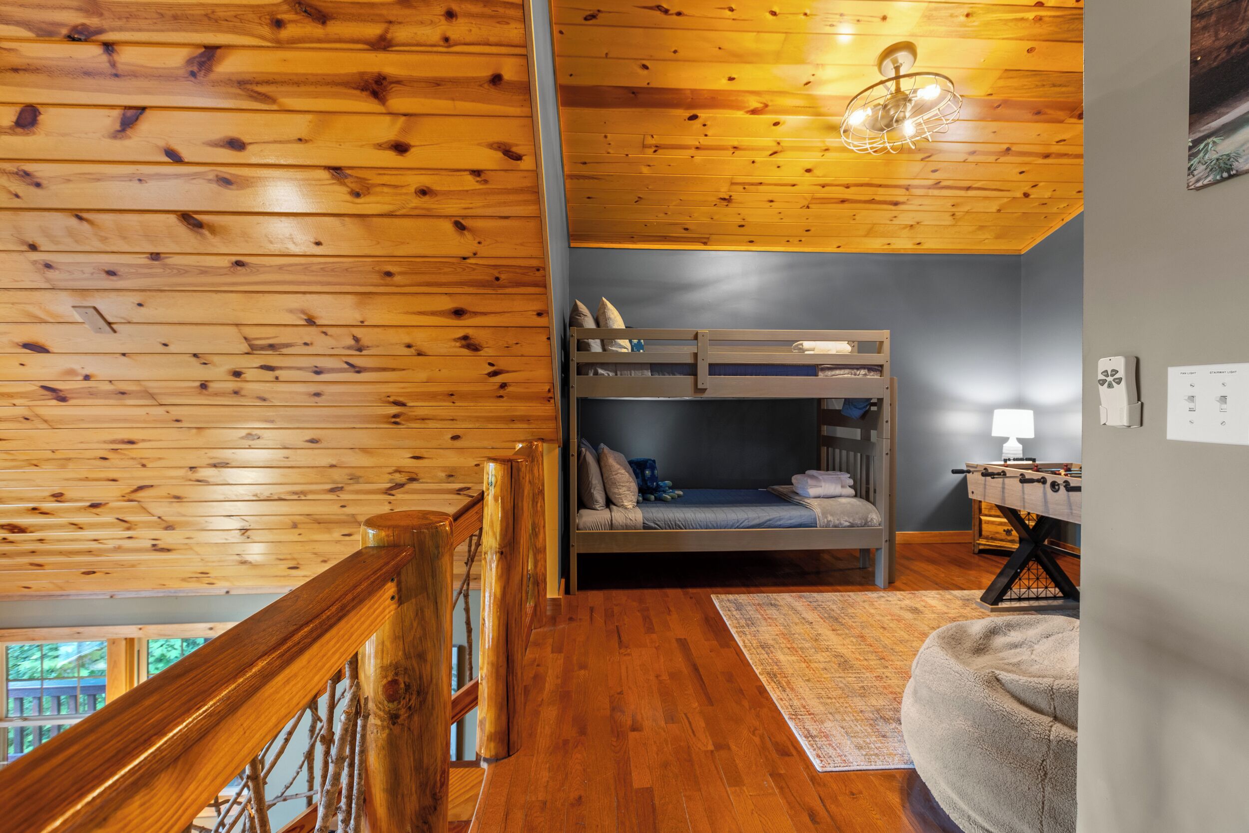 A wooden-floored room with bunk beds, a foosball table, and a view of the outdoors.