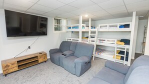 Une pièce avec un canapé gris, un meuble de rangement en bois pour l’équipement audiovisuel et un lit superposé blanc avec espace de rangement.