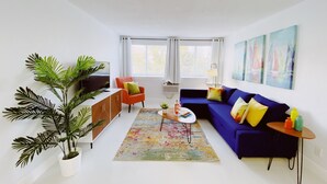 A modern living room with a blue sofa, orange armchair, and a large potted plant. - Spacious 2-Bed, 2-Bath in the Center of Miami w/ Free Parking (Miami)